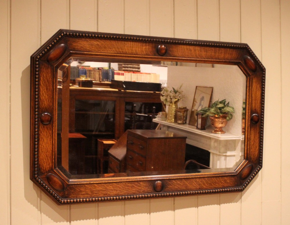 A large rectangular oak wall mirror with canted corners, beaded outer moulding, carved oval bosses, and a bevelled glass plate. View II