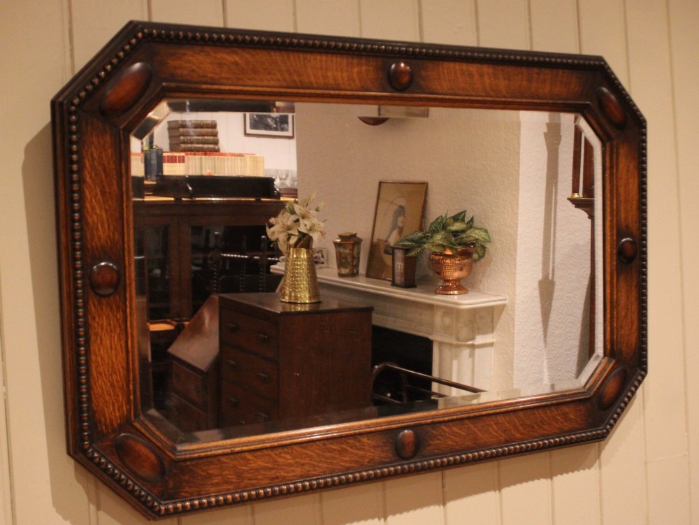 A large rectangular oak wall mirror with canted corners, beaded outer moulding, carved oval bosses, and a bevelled glass plate. View V