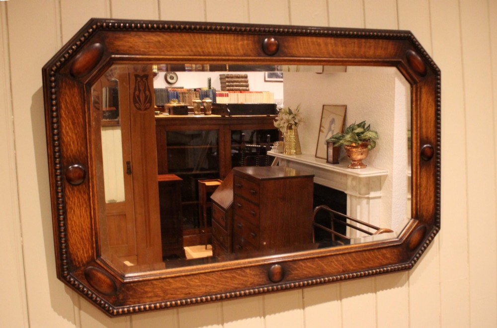 A large rectangular oak wall mirror with canted corners, beaded outer moulding, carved oval bosses, and a bevelled glass plate. View IX