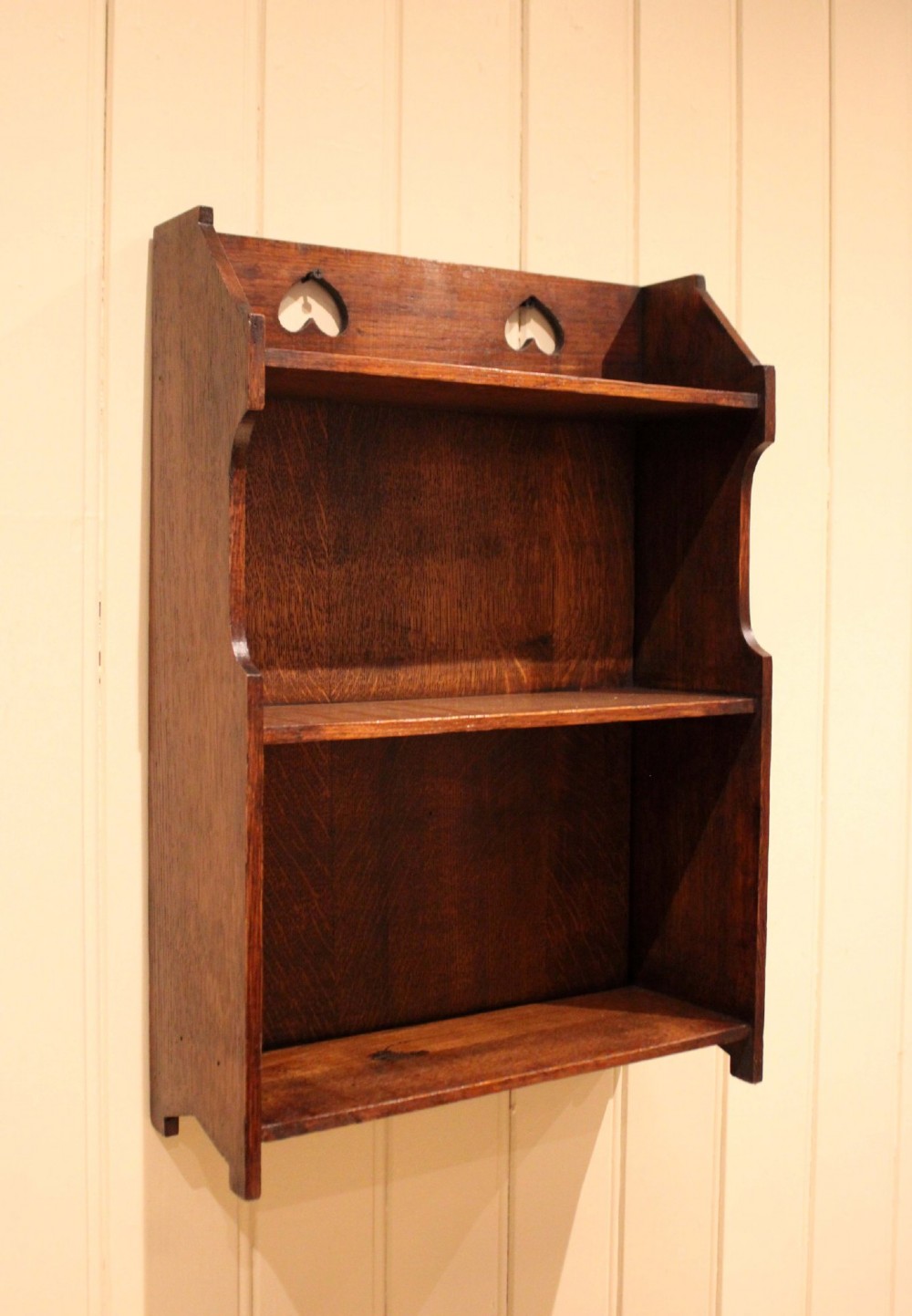 Dark oak Arts and Crafts three-tier wall shelving unit with two pierced heart cut-outs along the upper gallery rail. View IV