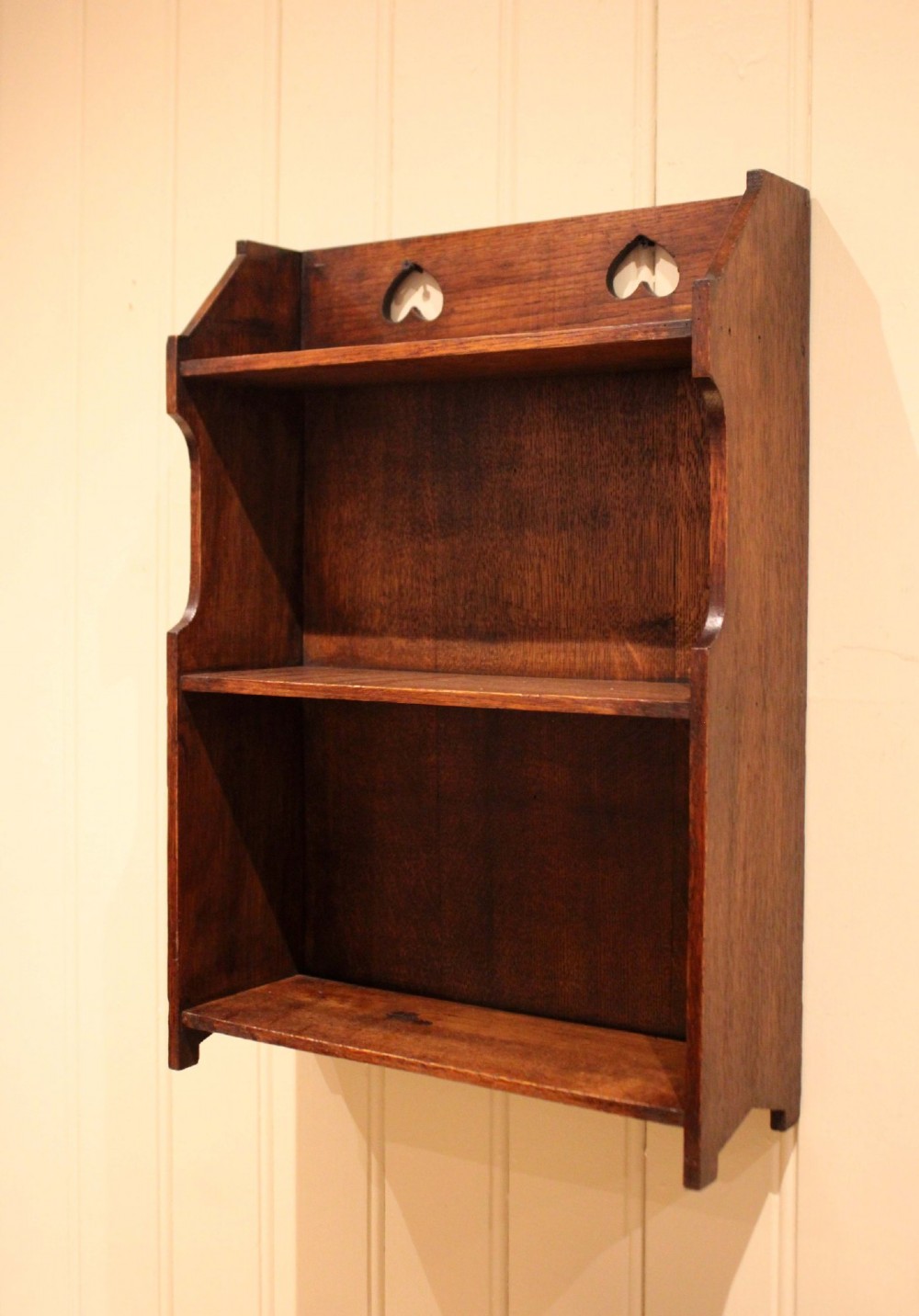 Dark oak Arts and Crafts three-tier wall shelving unit with two pierced heart cut-outs along the upper gallery rail. View VI