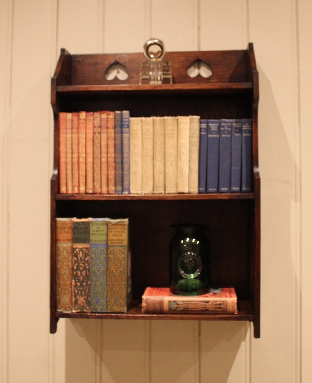 Dark oak Arts and Crafts three-tier wall shelving unit with two pierced heart cut-outs along the upper gallery rail. View VII
