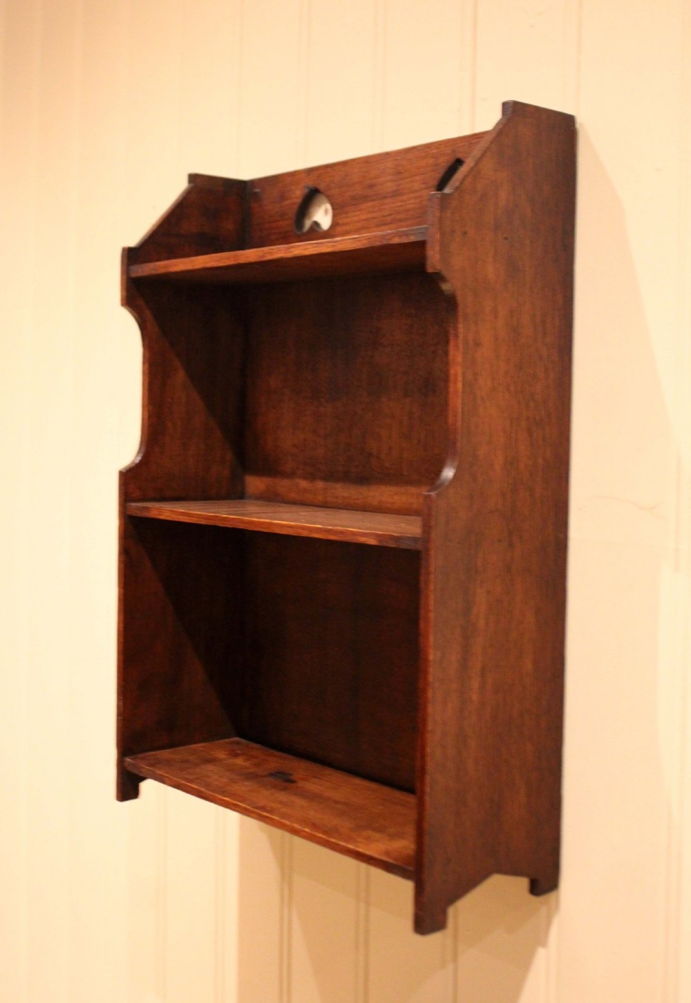 Dark oak Arts and Crafts three-tier wall shelving unit with two pierced heart cut-outs along the upper gallery rail. View VIII