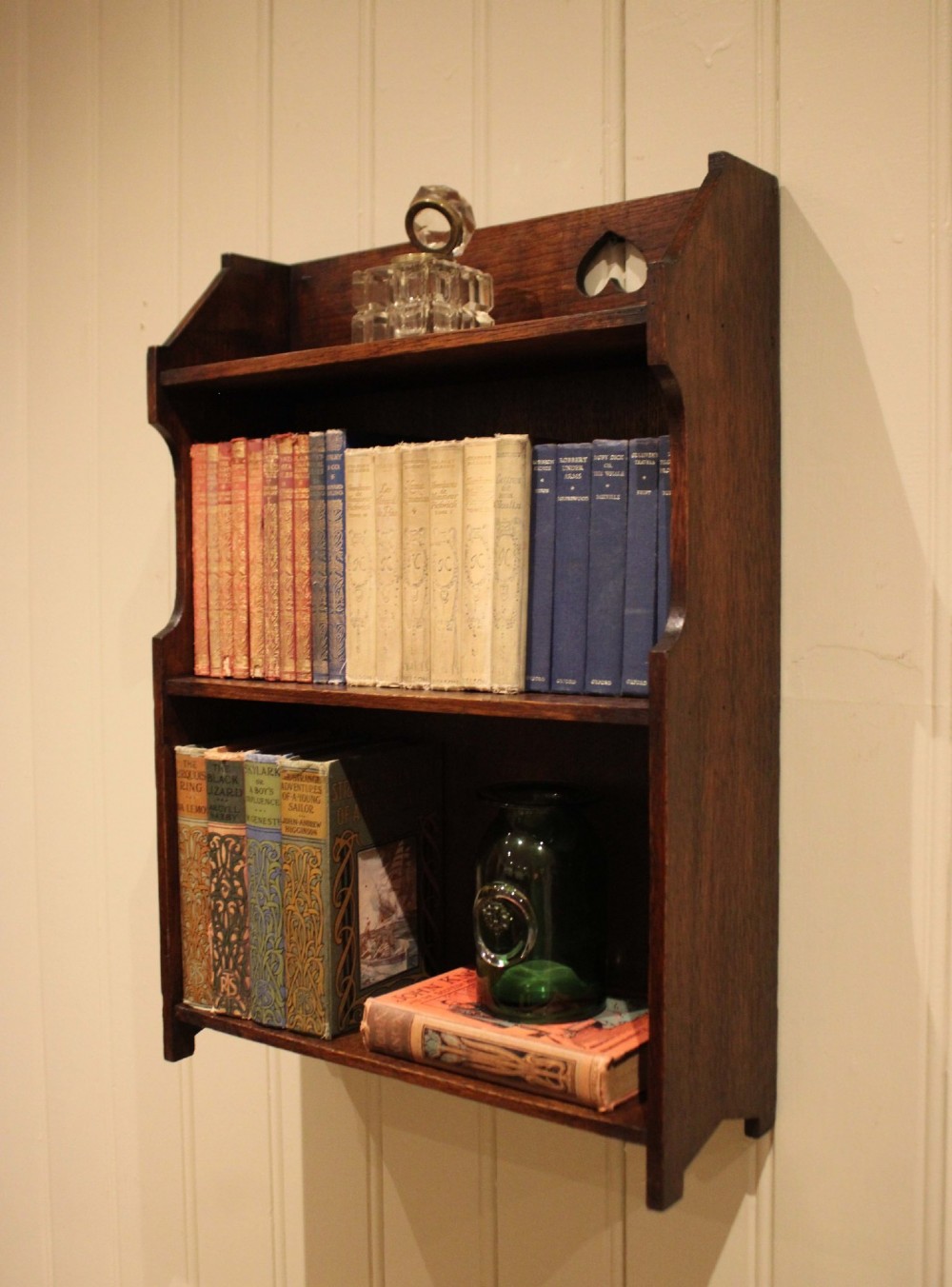 Dark oak Arts and Crafts three-tier wall shelving unit with two pierced heart cut-outs along the upper gallery rail. View IX