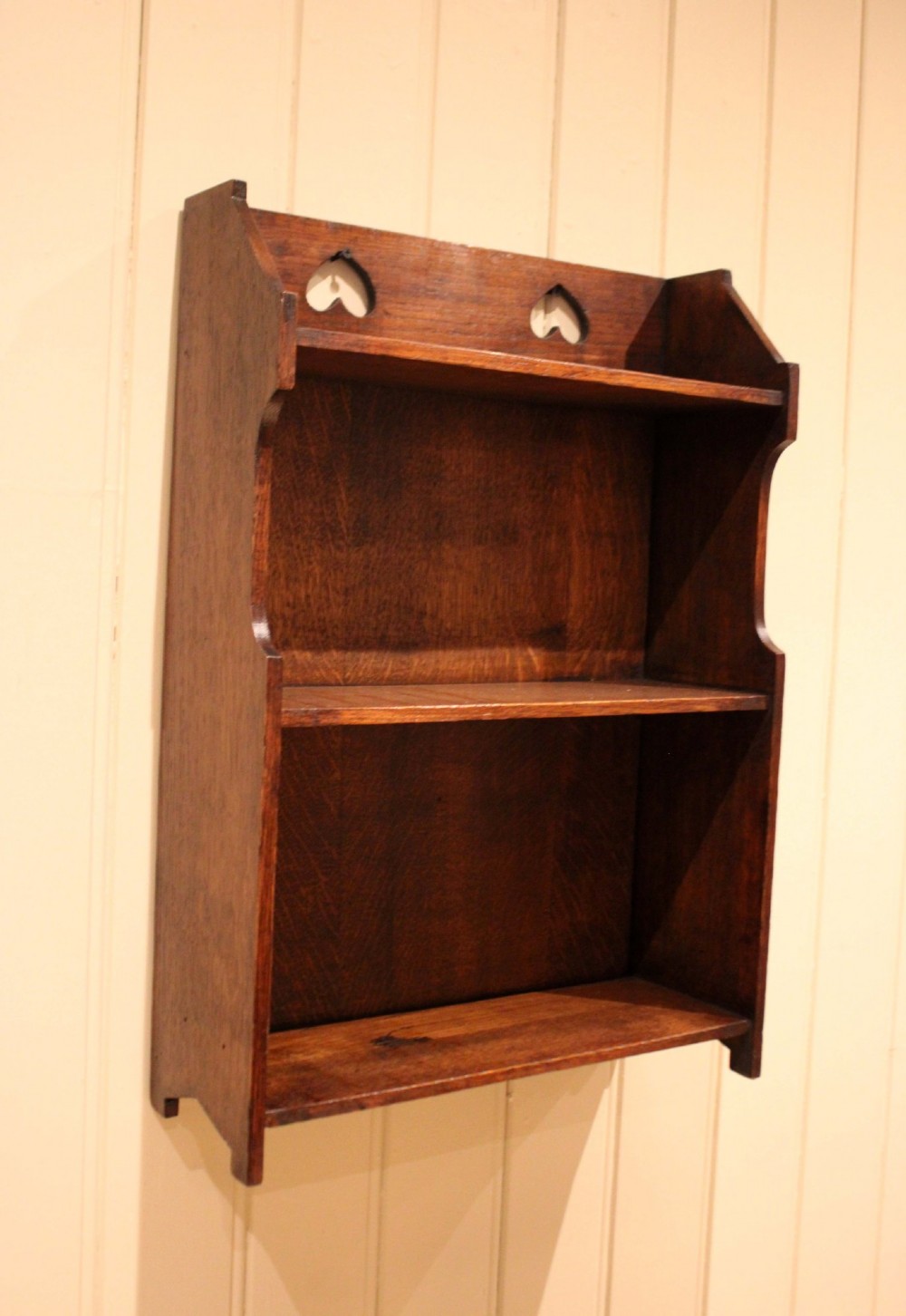 Dark oak Arts and Crafts three-tier wall shelving unit with two pierced heart cut-outs along the upper gallery rail. View X