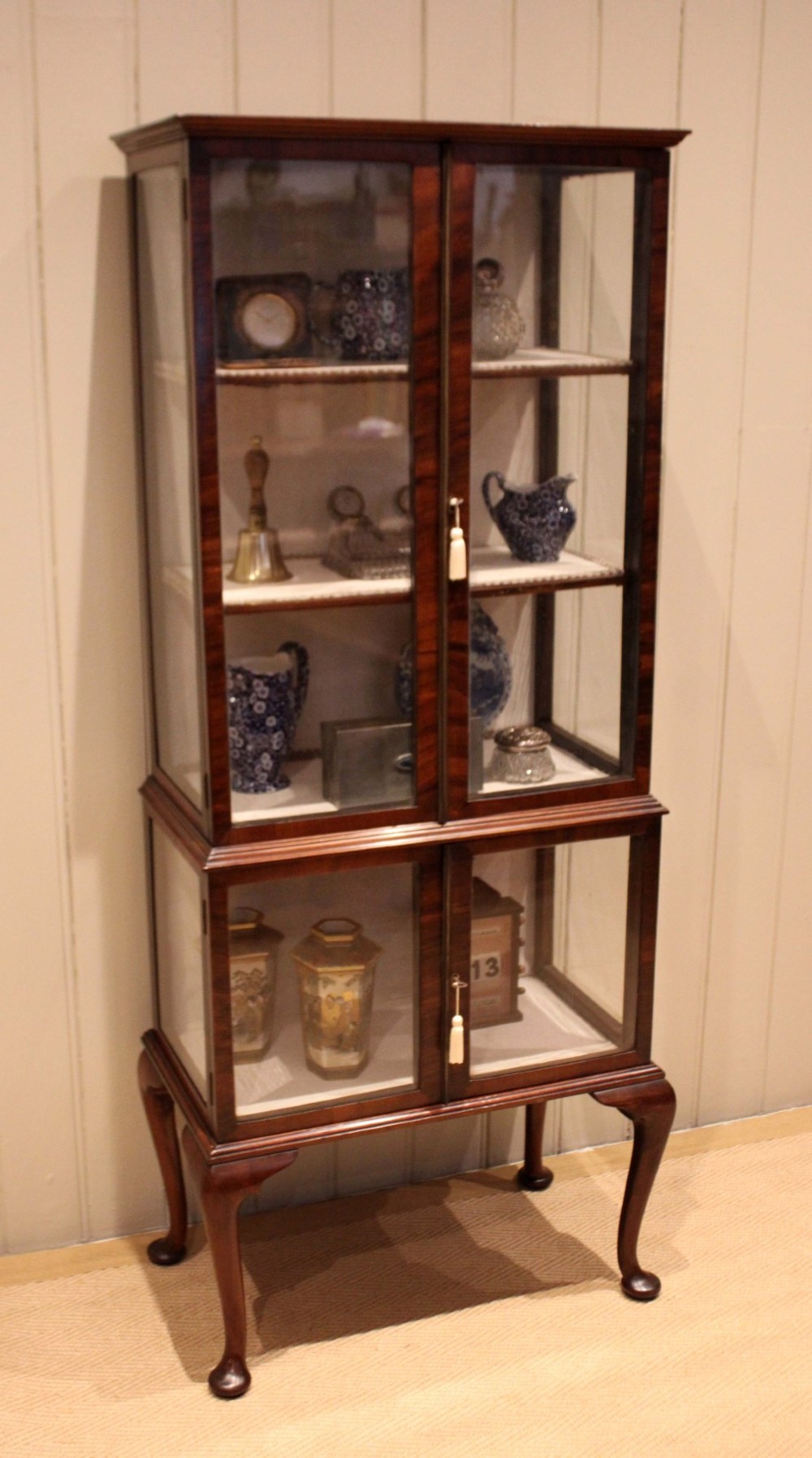 An Edwardian dark mahogany display cabinet with glazed doors and sides, resting on cabriole legs with pad feet.