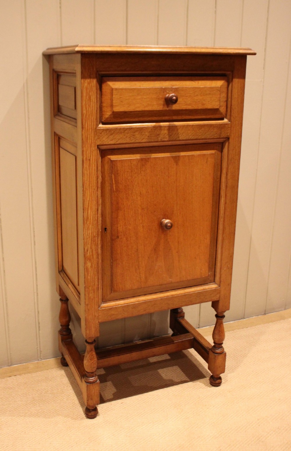 An Edwardian oak side cabinet featuring a single top drawer over a cupboard door with turned wooden knobs and turned legs.