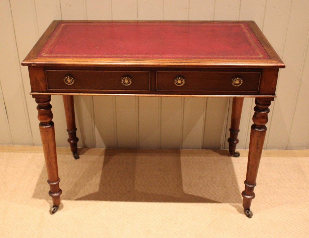 A late 19th-century mahogany writing desk featuring a red gold-tooled leather writing surface, two drawers with brass ring handles, and turned legs on brass castors.