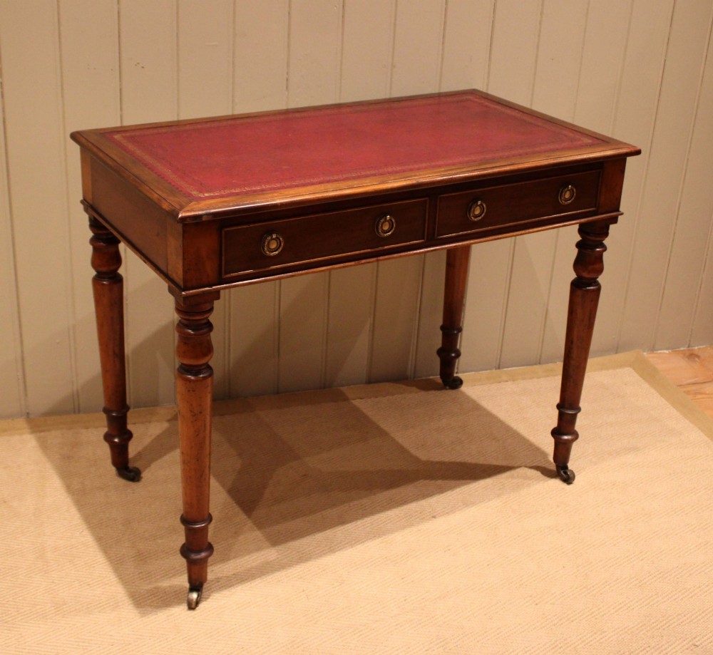 A late 19th-century mahogany writing desk featuring a red gold-tooled leather writing surface, two drawers with brass ring handles, and turned legs on brass castors. View II