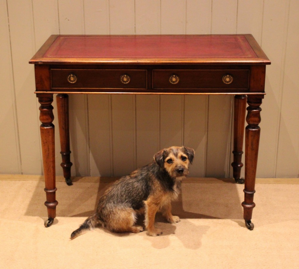 A late 19th-century mahogany writing desk featuring a red gold-tooled leather writing surface, two drawers with brass ring handles, and turned legs on brass castors. View III