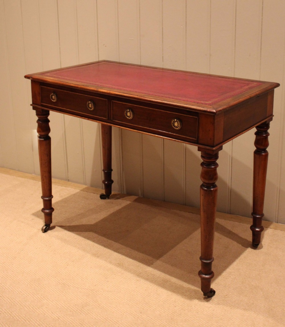 A late 19th-century mahogany writing desk featuring a red gold-tooled leather writing surface, two drawers with brass ring handles, and turned legs on brass castors. View IV