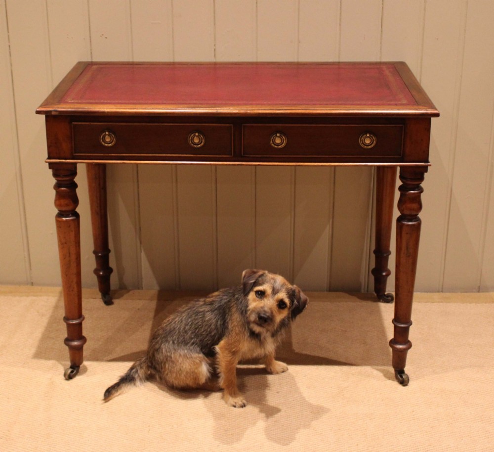 A late 19th-century mahogany writing desk featuring a red gold-tooled leather writing surface, two drawers with brass ring handles, and turned legs on brass castors. View V
