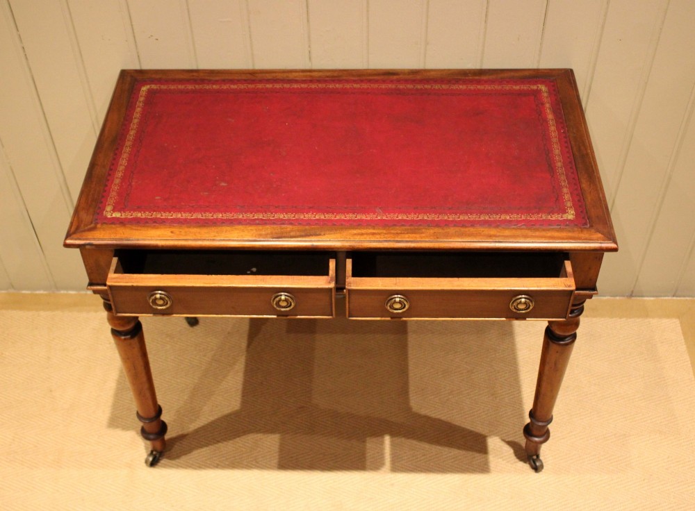 A late 19th-century mahogany writing desk featuring a red gold-tooled leather writing surface, two drawers with brass ring handles, and turned legs on brass castors. View VI