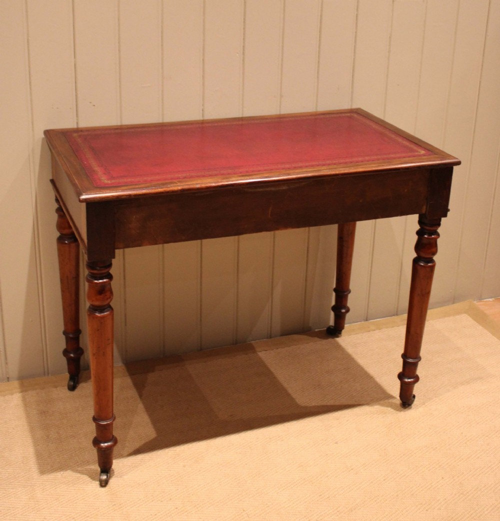 A late 19th-century mahogany writing desk featuring a red gold-tooled leather writing surface, two drawers with brass ring handles, and turned legs on brass castors. View VII