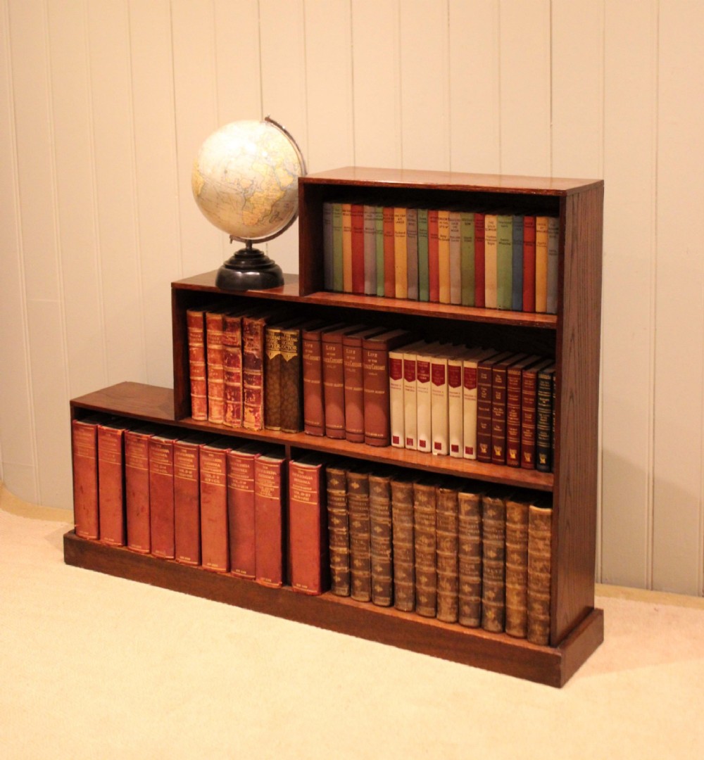 A stepped medium brown oak sectional bookcase with three open tiered shelves arranged in an asymmetrical stair-like configuration.