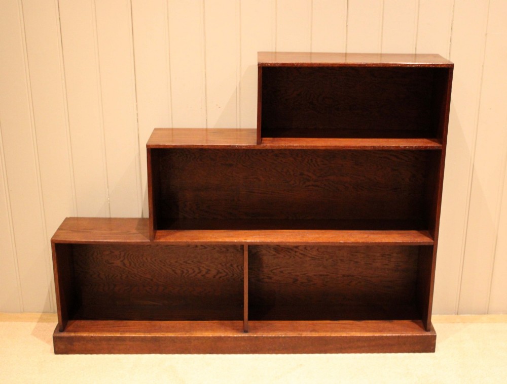 A stepped medium brown oak sectional bookcase with three open tiered shelves arranged in an asymmetrical stair-like configuration. View II