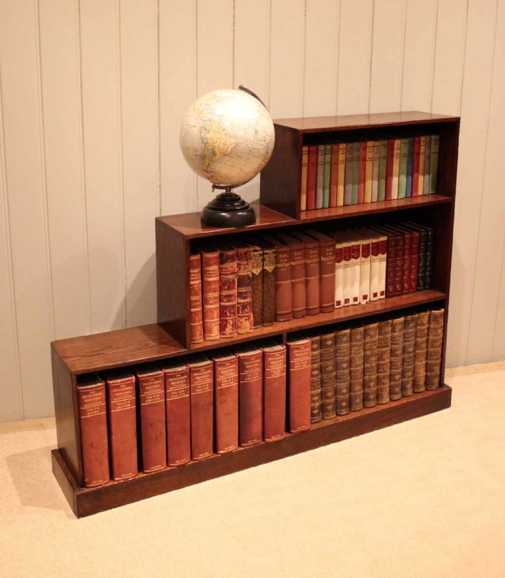 A stepped medium brown oak sectional bookcase with three open tiered shelves arranged in an asymmetrical stair-like configuration. View III