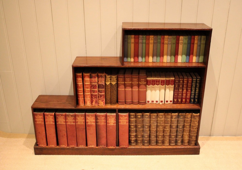 A stepped medium brown oak sectional bookcase with three open tiered shelves arranged in an asymmetrical stair-like configuration. View V