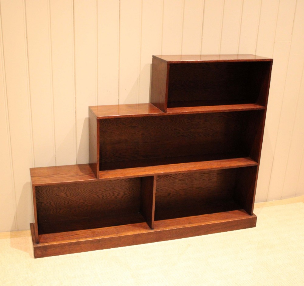 A stepped medium brown oak sectional bookcase with three open tiered shelves arranged in an asymmetrical stair-like configuration. View VI
