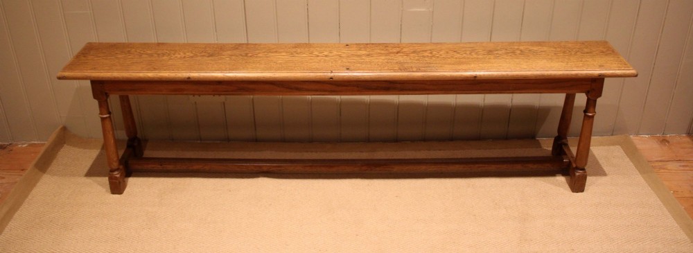 A long rectangular solid oak bench featuring turned legs connected by a low stretcher rail.