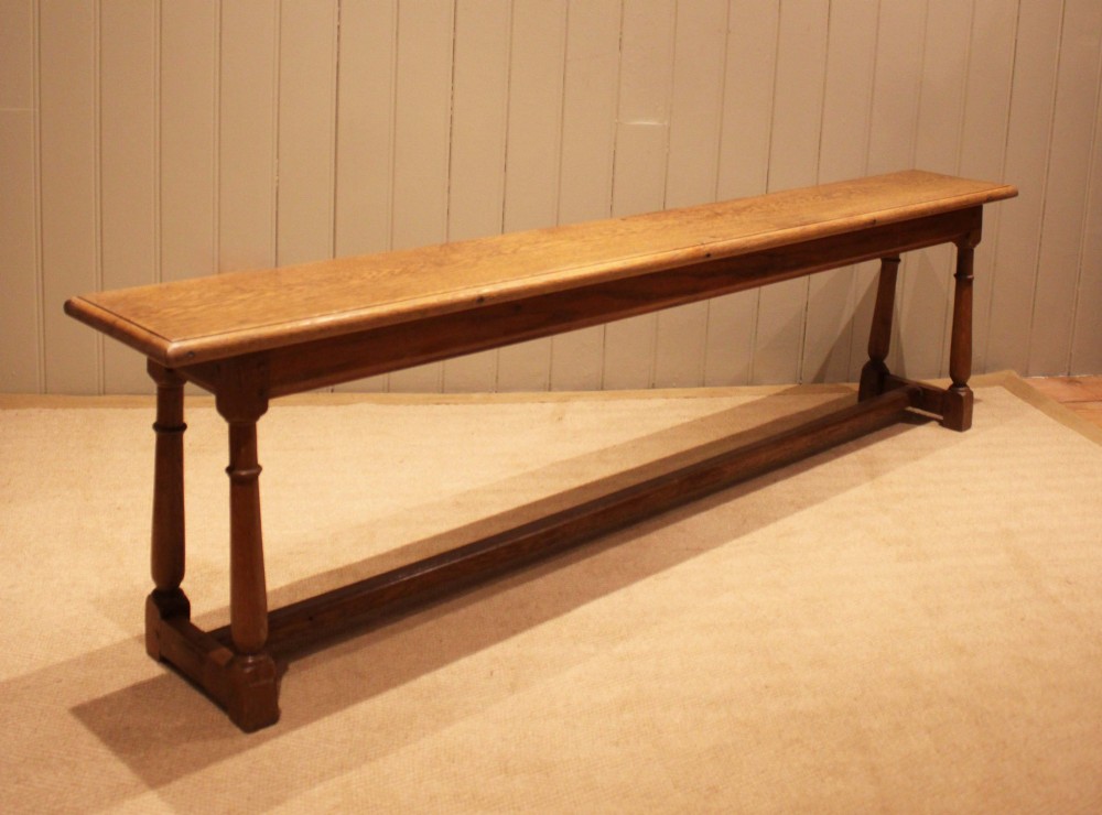 A long rectangular solid oak bench featuring turned legs connected by a low stretcher rail. View II