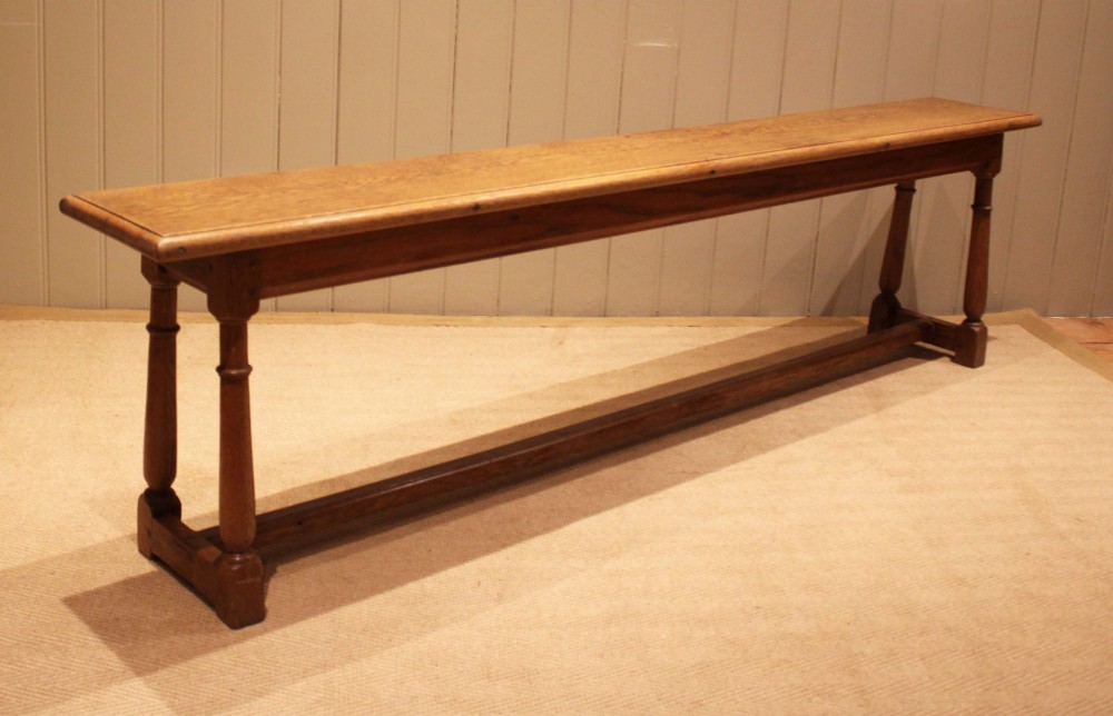 A long rectangular solid oak bench featuring turned legs connected by a low stretcher rail. View VII