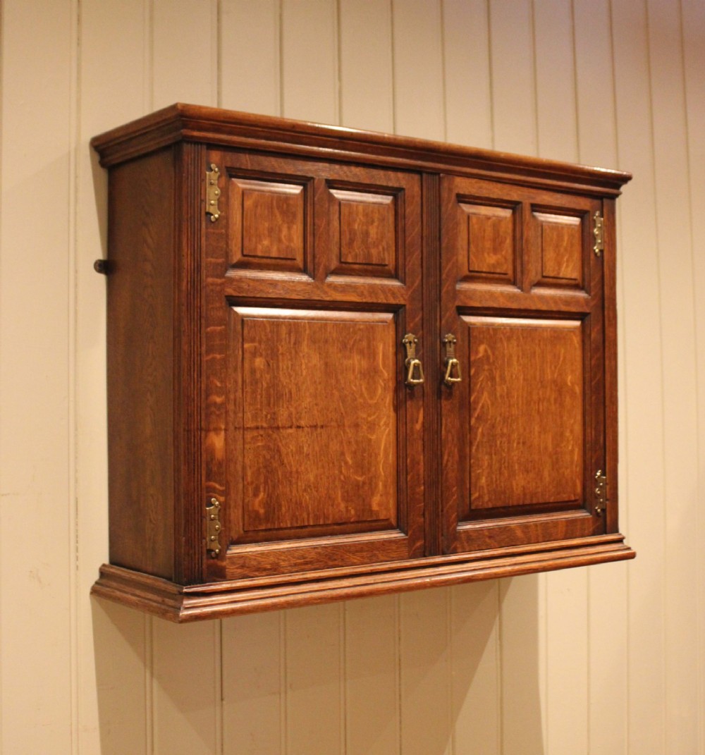 A late nineteenth-century solid oak wall cabinet featuring panelled double doors with brass hinges and handles.