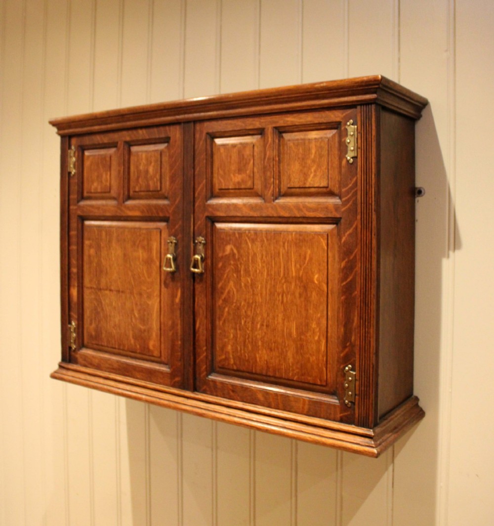A late nineteenth-century solid oak wall cabinet featuring panelled double doors with brass hinges and handles. View II