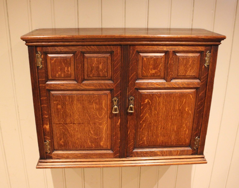 A late nineteenth-century solid oak wall cabinet featuring panelled double doors with brass hinges and handles. View III