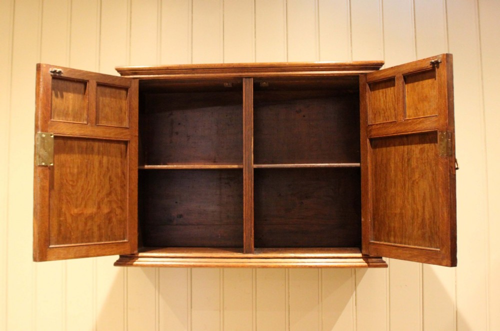 A late nineteenth-century solid oak wall cabinet featuring panelled double doors with brass hinges and handles. View IV
