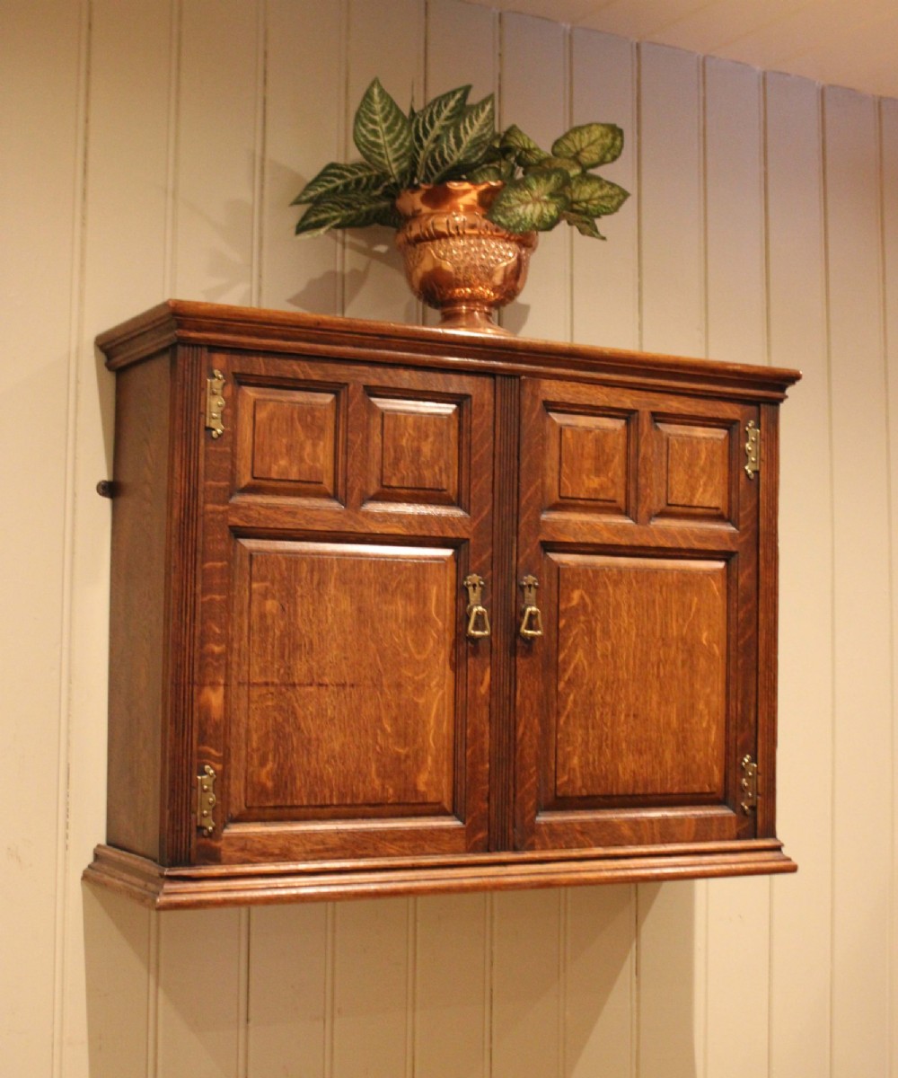 A late nineteenth-century solid oak wall cabinet featuring panelled double doors with brass hinges and handles. View V
