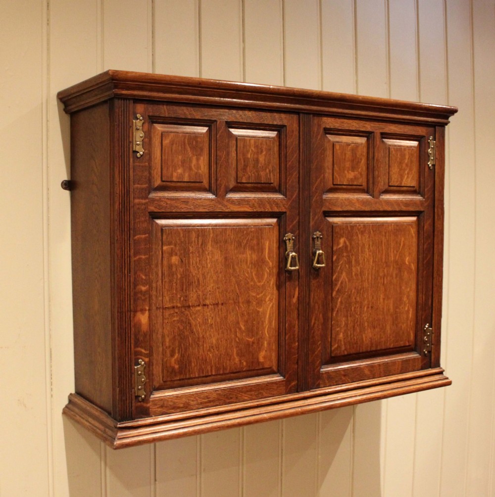 A late nineteenth-century solid oak wall cabinet featuring panelled double doors with brass hinges and handles. View VI