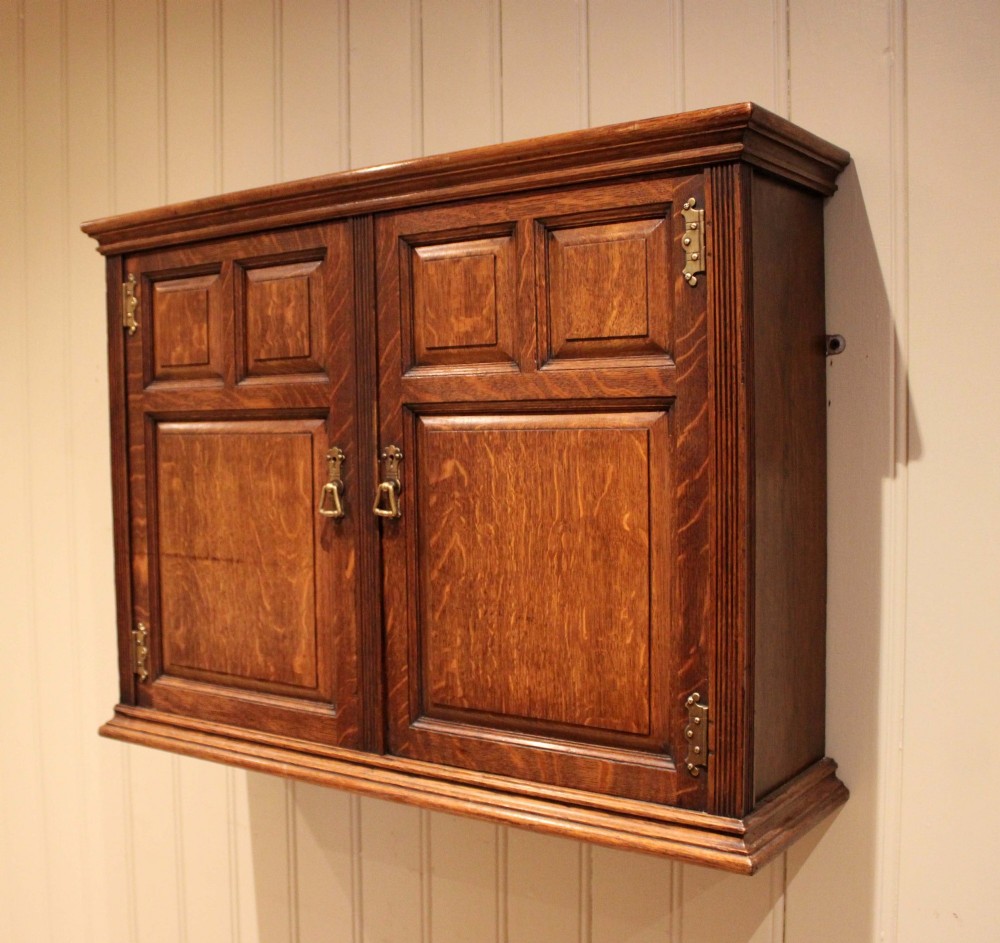 A late nineteenth-century solid oak wall cabinet featuring panelled double doors with brass hinges and handles. View VII