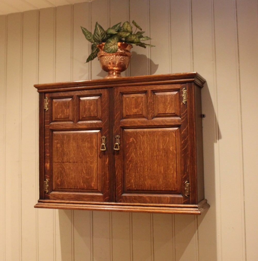 A late nineteenth-century solid oak wall cabinet featuring panelled double doors with brass hinges and handles. View IX