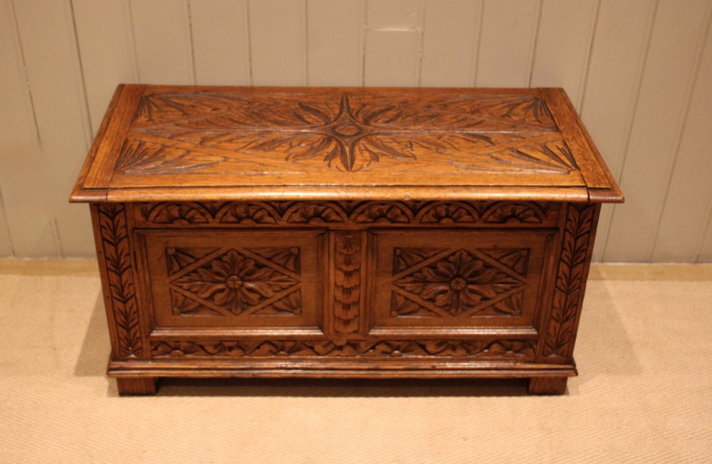 A solid golden oak coffer with detailed foliate and starburst hand-carvings across the hinged lid and front twin panels.