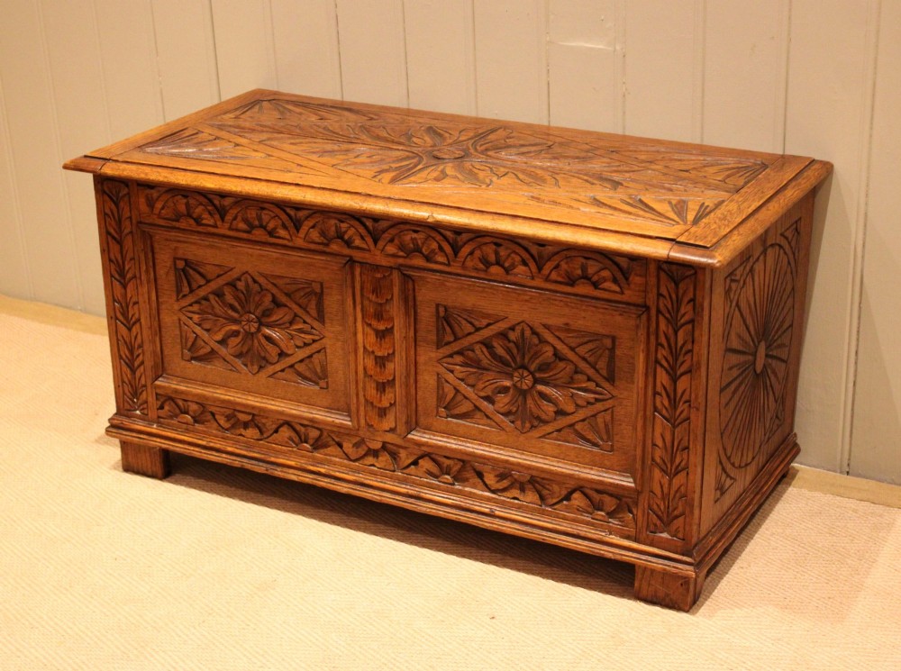 A solid golden oak coffer with detailed foliate and starburst hand-carvings across the hinged lid and front twin panels. View II