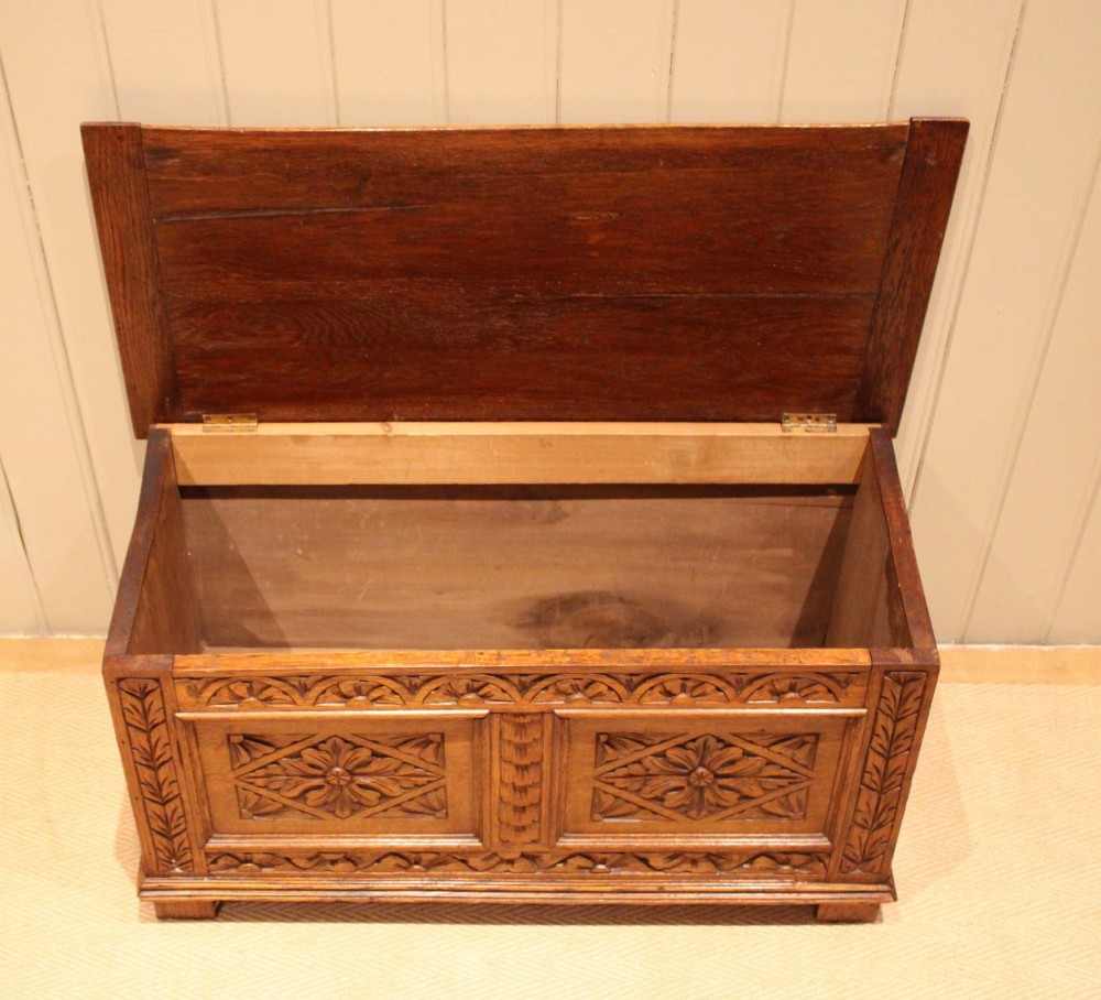 A solid golden oak coffer with detailed foliate and starburst hand-carvings across the hinged lid and front twin panels. View III
