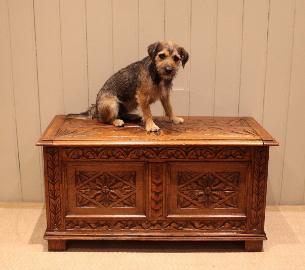 A solid golden oak coffer with detailed foliate and starburst hand-carvings across the hinged lid and front twin panels. View IV