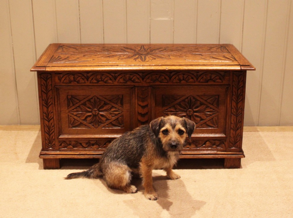 A solid golden oak coffer with detailed foliate and starburst hand-carvings across the hinged lid and front twin panels. View V