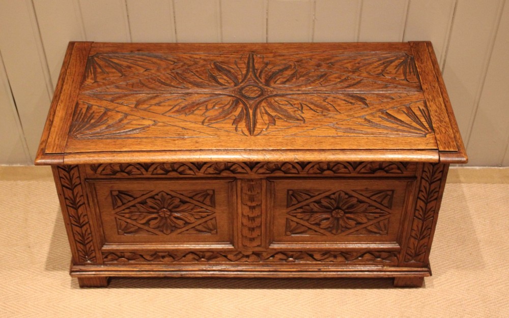 A solid golden oak coffer with detailed foliate and starburst hand-carvings across the hinged lid and front twin panels. View VI