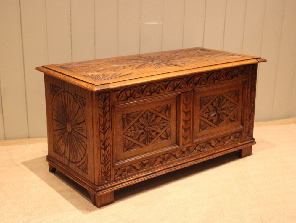 A solid golden oak coffer with detailed foliate and starburst hand-carvings across the hinged lid and front twin panels. View VII