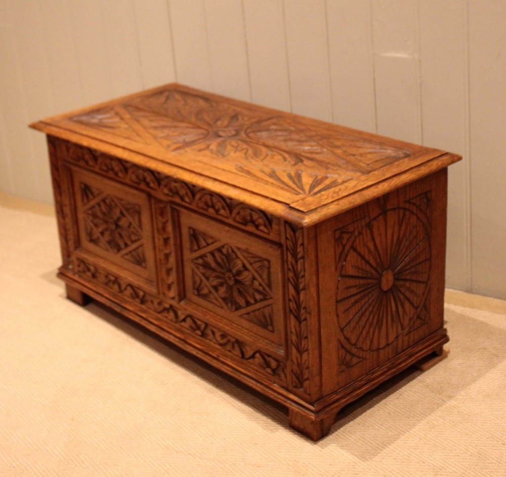 A solid golden oak coffer with detailed foliate and starburst hand-carvings across the hinged lid and front twin panels. View VIII