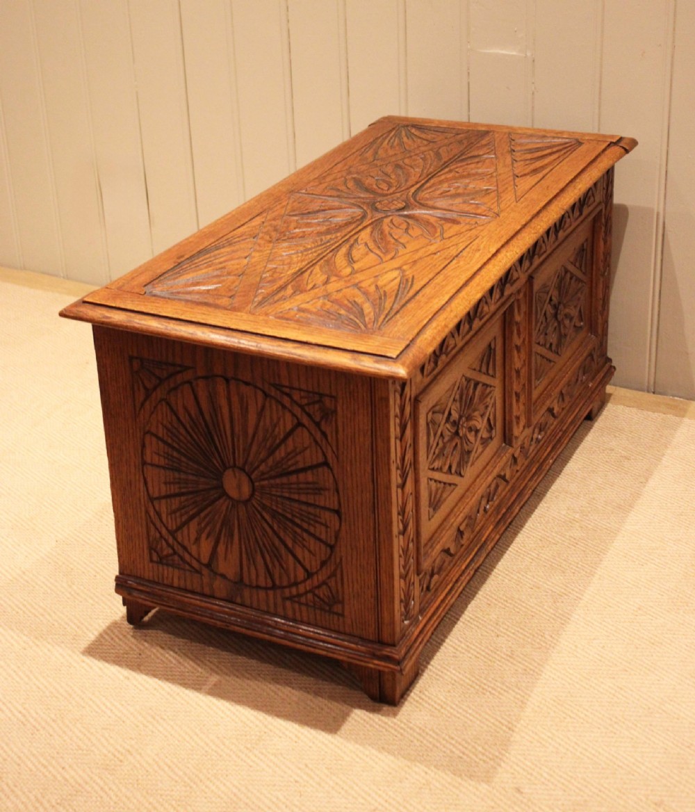 A solid golden oak coffer with detailed foliate and starburst hand-carvings across the hinged lid and front twin panels. View IX