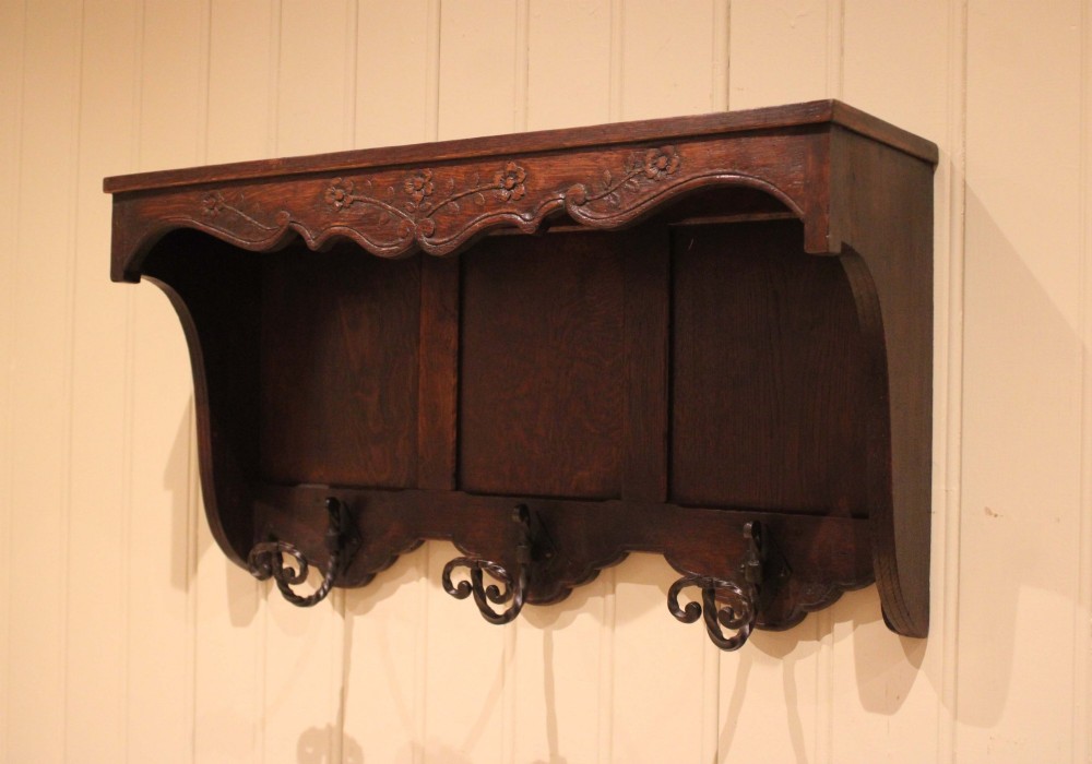 A dark oak wall-mounted coat rack featuring a top shelf, a carved floral apron, a three-panel backboard, and three metal coat hooks. View II