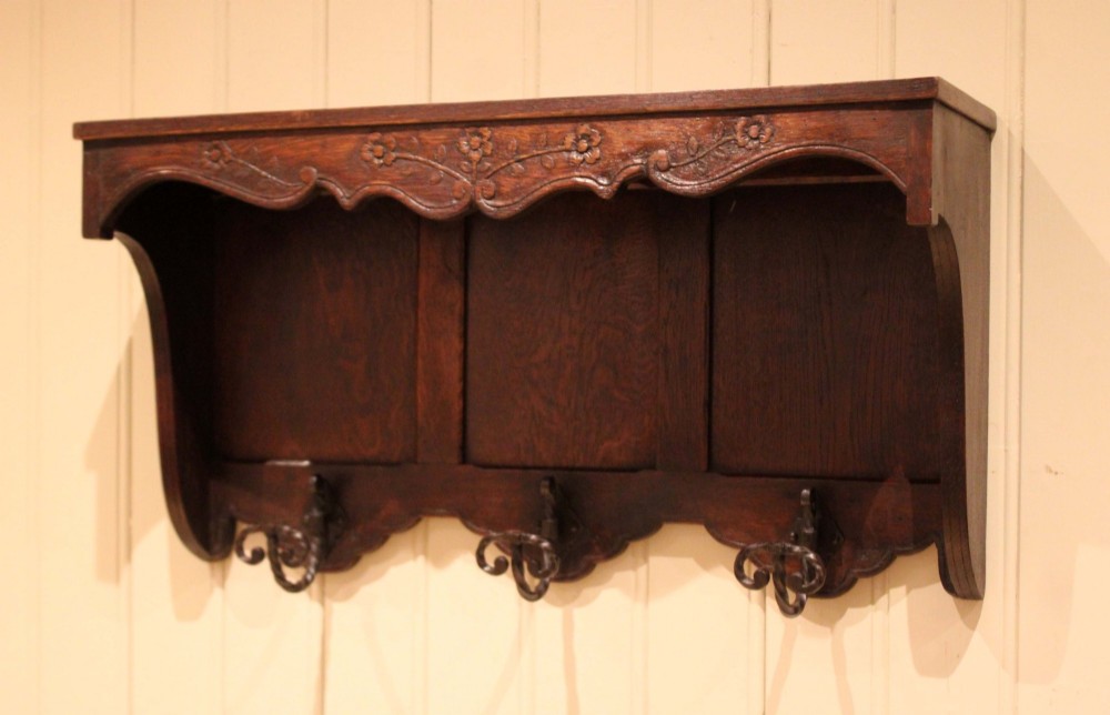 A dark oak wall-mounted coat rack featuring a top shelf, a carved floral apron, a three-panel backboard, and three metal coat hooks. View VIII