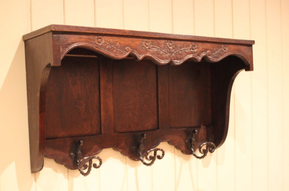 A dark oak wall-mounted coat rack featuring a top shelf, a carved floral apron, a three-panel backboard, and three metal coat hooks. View IX