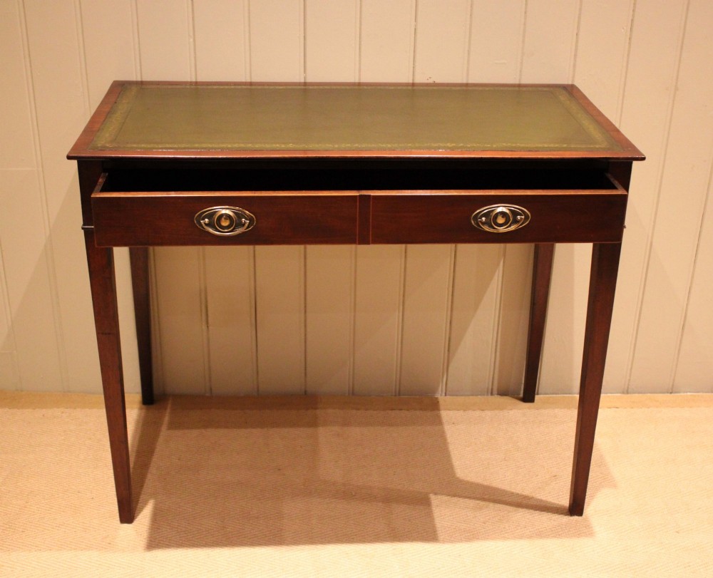 An early 19th-century mahogany writing desk featuring a green leather inset top, two frieze drawers with brass oval handles, and square tapered legs. View VI
