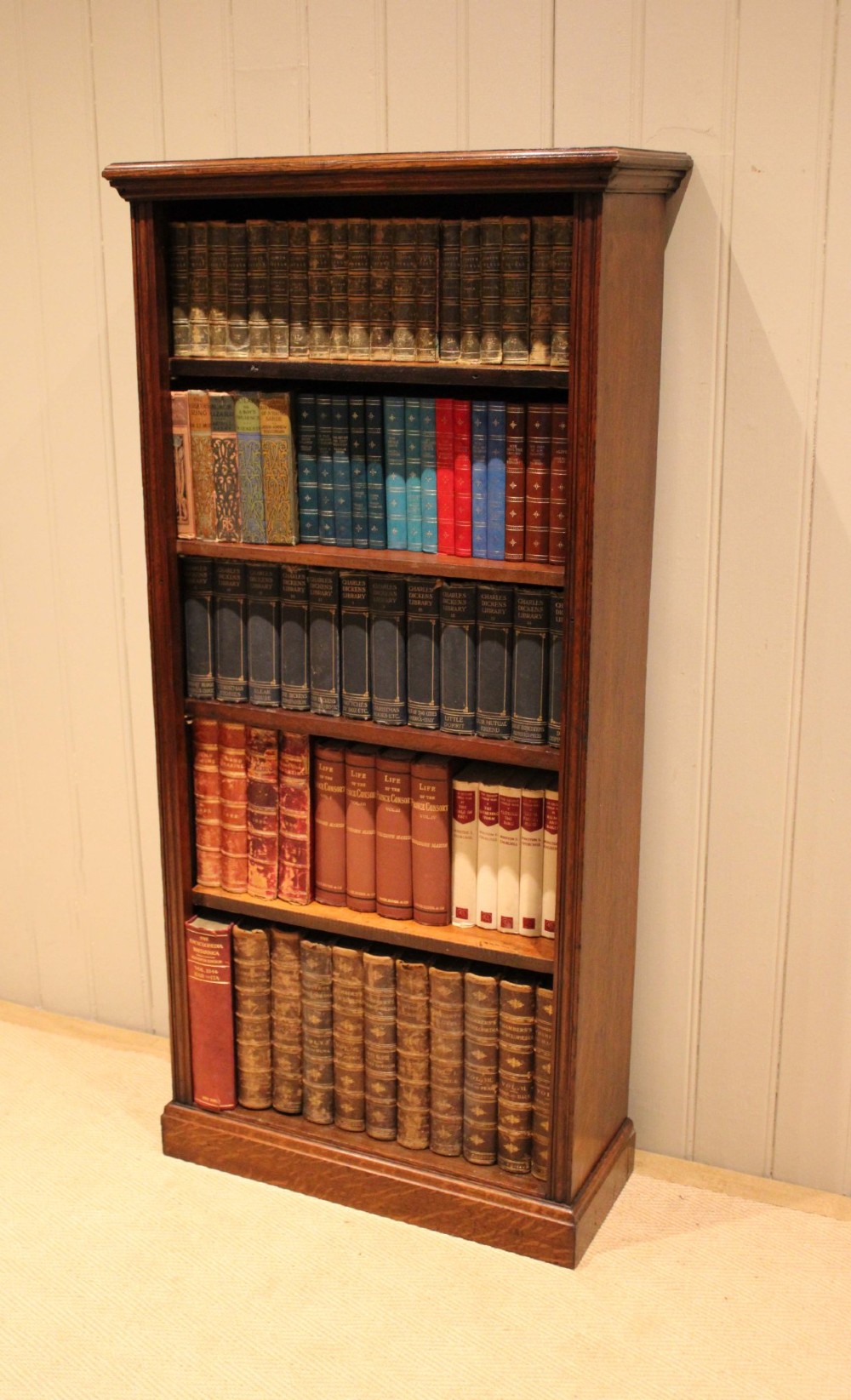 A tall late Victorian open oak bookcase featuring five adjustable shelves filled with books, a moulded top cornice, and a solid plinth base.