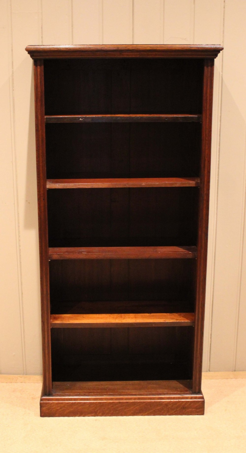 A tall late Victorian open oak bookcase featuring five adjustable shelves filled with books, a moulded top cornice, and a solid plinth base. View II