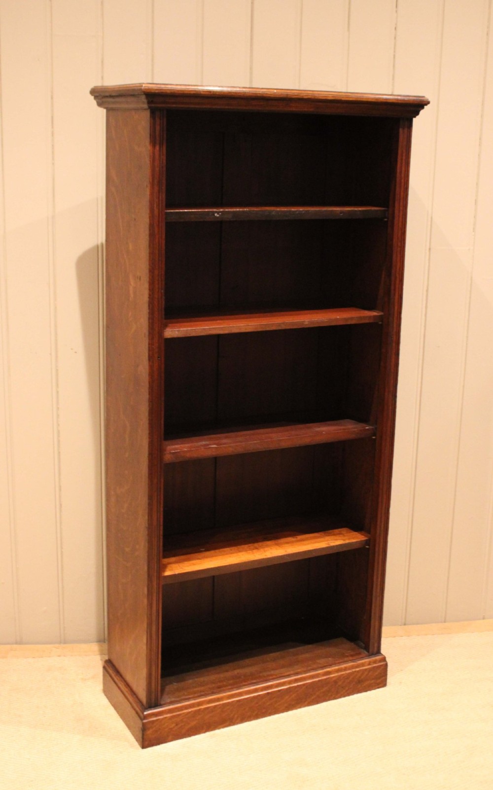 A tall late Victorian open oak bookcase featuring five adjustable shelves filled with books, a moulded top cornice, and a solid plinth base. View IV